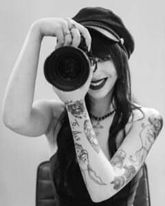 Portrait of a tattooed woman photographer smiling and posing with camera.
